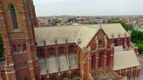 Aerial-view-of-a-beautiful-old-Church,-Beautiful-trees-and-grass-around-the-Church,-Pigeons-flying-over-the-Church,-People-stood-outside-the-Church