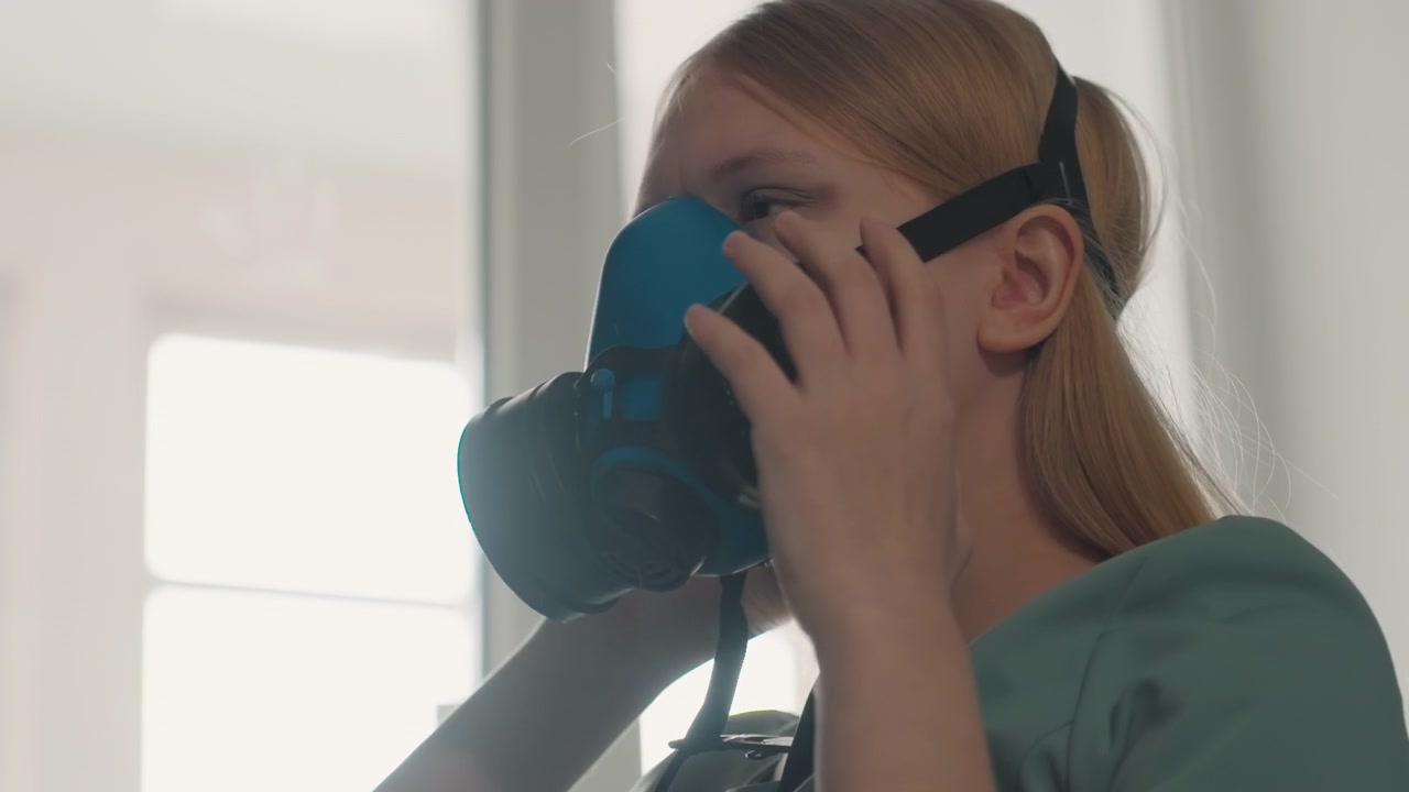 Donna che regola la cinghia della maschera per un compito di pulizia. Scena interna di donna che prepara con cura una maschera protettiva. Donna sicura che assicura la corretta aderenza del respiratore per l'attività di pulizia domestica