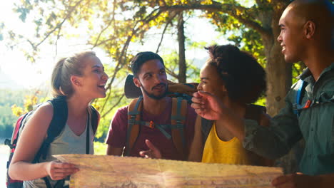 group of friends with backpacks looking at map on vacation hiking through forest countryside