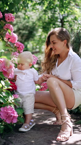 happy mother and her little baby son near the blossoming bush. cute kid touches the flowers happily. vertical video.
