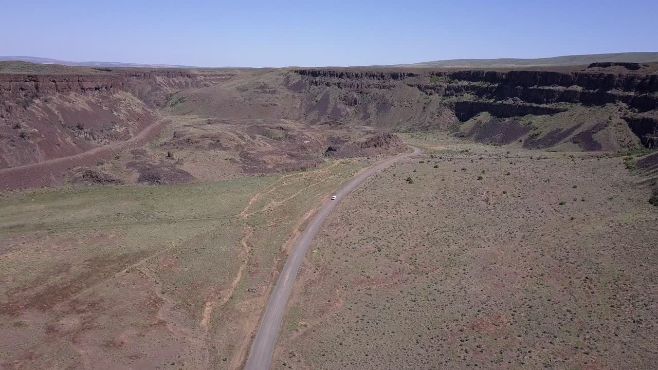 aerial: vehículo solitario conduce camino solitario a través de scablands canyon, wa