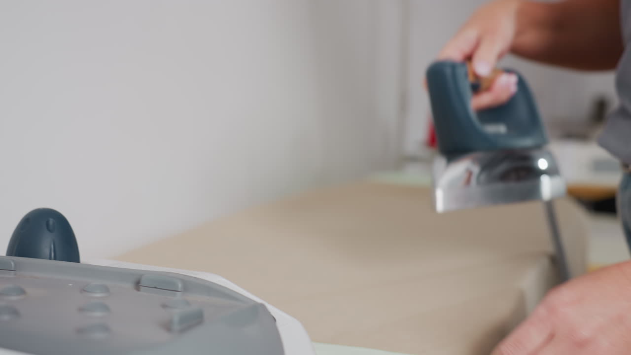 Close up of dress maker picking iron, placing on apparel, steam visibly rising, removing wrinkles, ensuring neat finish, highlighting professional pressing skill, focusing on careful technique