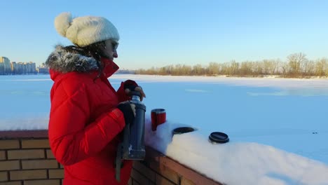 young woman pouring tea or coffee in winter park. winter woman