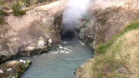 Waves-of-hot-water-are-ejected-from-the-Dragon's-Mouth-Spring-and-camera-tilts-up-with-rising-steam