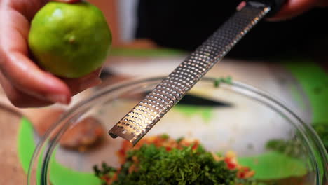 zesting a lime over a special homemade recipe with the ingredients in a bowl with a microplane grater