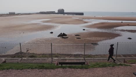 Woman-keeping-fit-with-a-brisk-walk-along-a-path-next-to-the-beach-with-sea-air