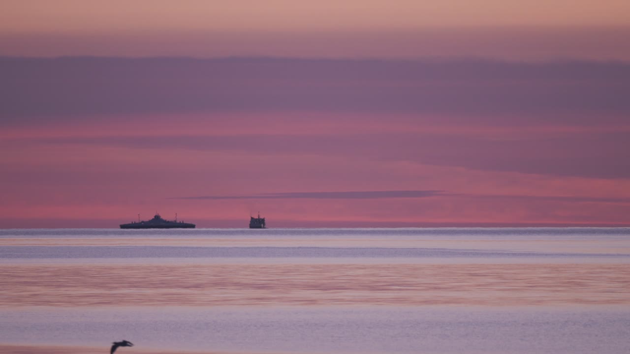 멀리 있는 배 와 페리 가 황혼 에 평온 한 물 에서 항해 하고, 눈에 띄는 보라색 과 분홍색 하늘 을 배경 으로 하고 있다