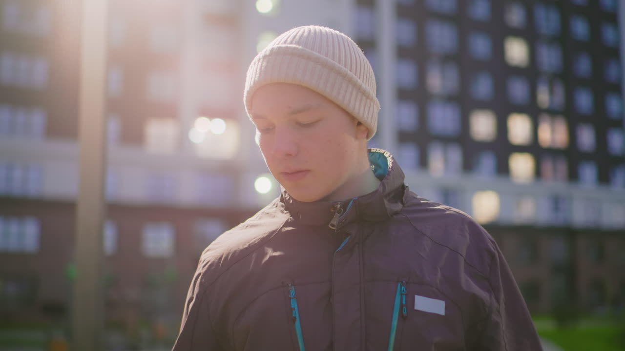 urban evening portrait white man wearing beanie, soft backlight and shallow depth, apartment window bokeh and gentle lens flare, hands tucked in jacket, candid shifts in gaze conveying student