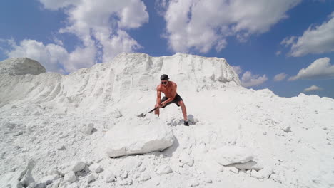 sportsman with huge hammer outdoors. sporty man demolishing big white rock by metal tool on the top of mountain in summer day. slow motion.