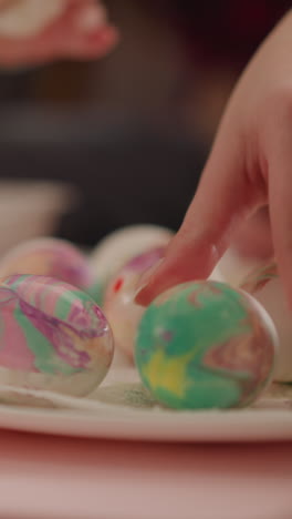 mother and daughter put decorated eggs to dry on square dish in room closeup slow motion. abru art traditions and christian holiday celebration