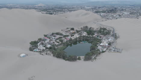 Drone shot revealing the city of Huacachina in Peru behind the dunes on a cloudy morning during the mist LOG