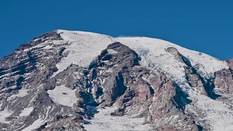 aerial drone video of a snow-covered, rocky mountain under clear skies, revealing dramatic glacial textures and geological formations
