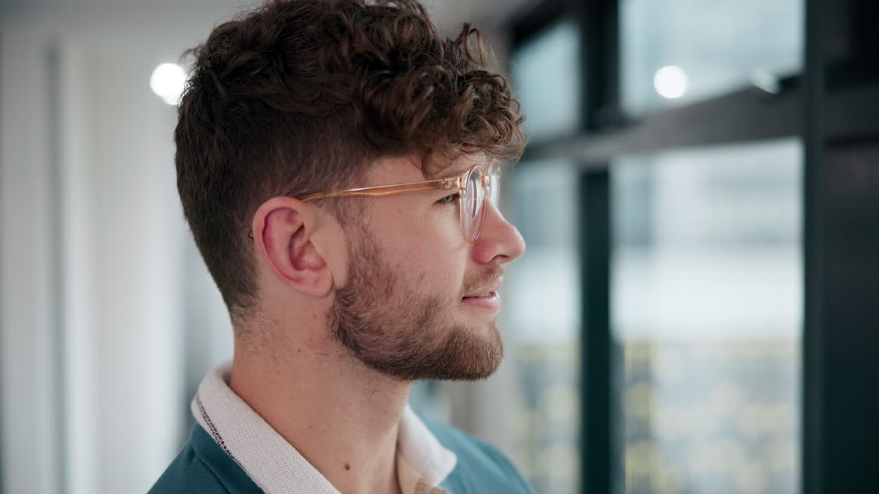 Man with curly hair and glasses looking out the window