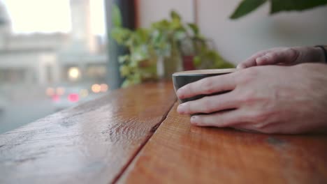 black coffee cup on wooden table overlooking street is raised to drink