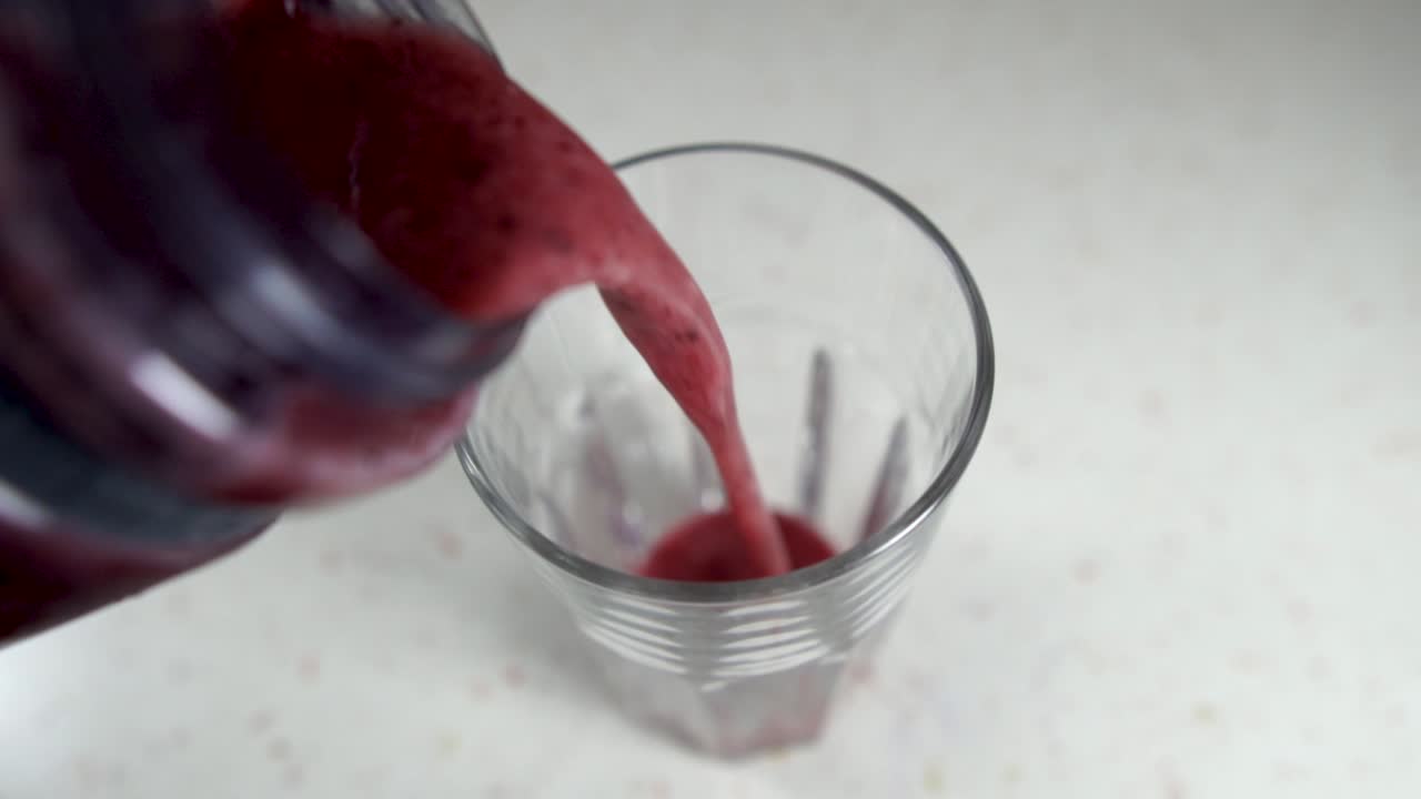 Pouring colorful forest fruit smoothie into a glass from a plastic jar, SLOW MOTION
