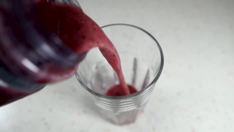 Pouring-colorful-forest-fruit-smoothie-into-a-glass-from-a-plastic-jar,-SLOW-MOTION