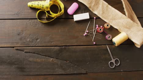 video of measure, scissors, chalk, pins, threads and hessian on wooden background with copy space