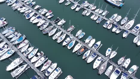 top down aerial view above luxury yachts parked on turquoise ocean water marina rotating right shot