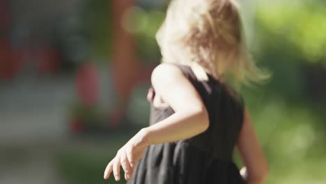 a fair-skinned blonde girl in a black dress runs through the garden carrying a bag