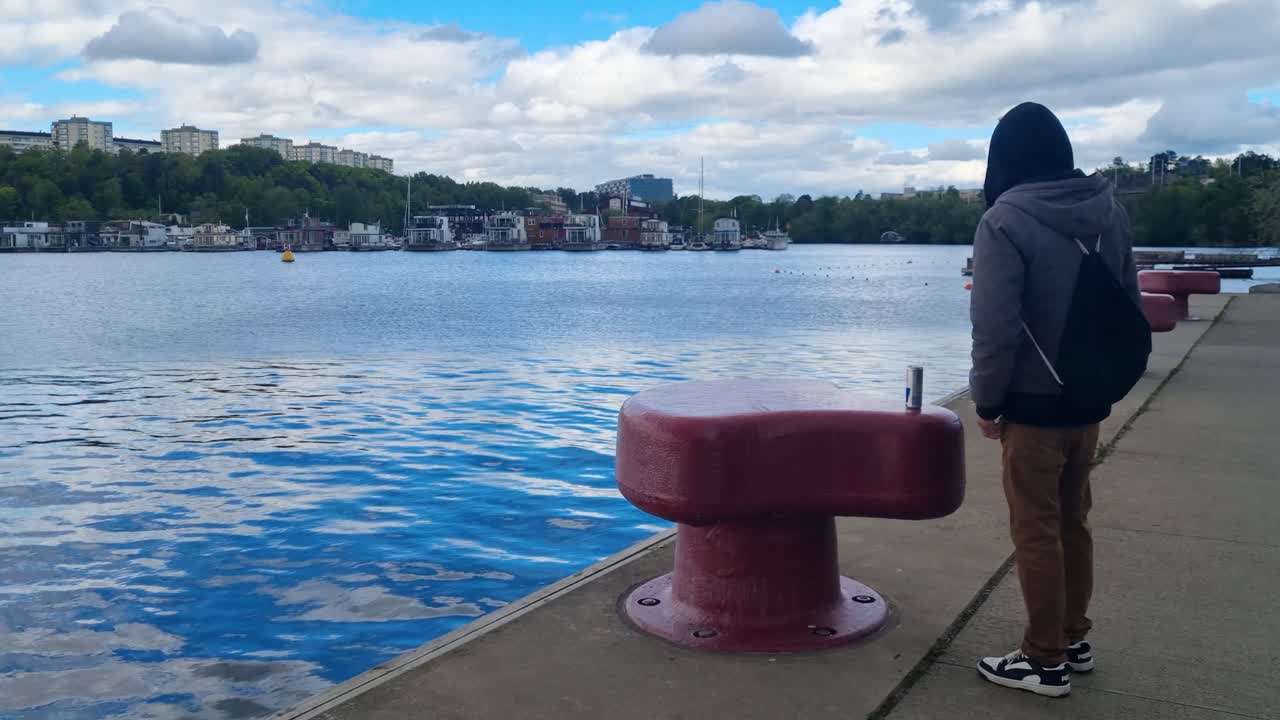 A lone man in a hoodie is taking pictures of the Ulvsundasjön bay in Stockholm, Sweden