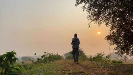 Hombre-Trotando-Al-Aire-Libre-En-El-Paisaje-Rural,-Puesta-De-Sol-En-El-Cielo-Brumoso,-Estático,-ángulo-Bajo