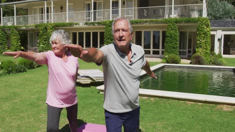 happy caucasian senior couple practicing yoga in garden standing and stretching in the sun