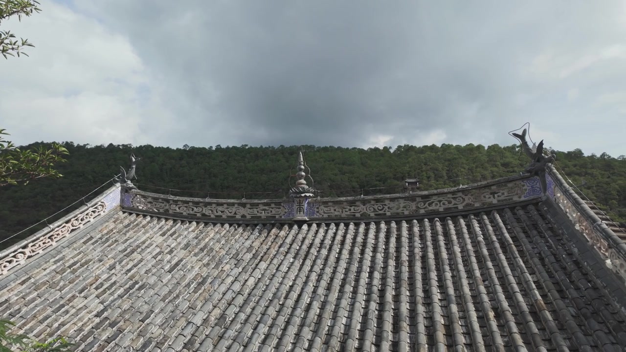 울창한 녹색 산림을 배경으로 복잡한 회색 기와와 장식 조각이 특징인 전통 아시아 사원 지붕의 시네마틱 클로즈업