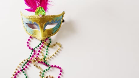 video of masquerade mask with pink feathers and mardi gras beads on white background with copy space