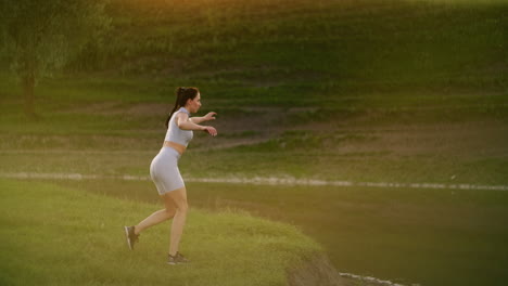 Una-Mujer-Entrena-En-La-Orilla-De-Un-Lago-En-Un-Parque-Bajo-La-Luz-Del-Sol-Del-Atardecer.-Estocada-Cruzada-Hacia-Atrás-Con-Un-Salto.