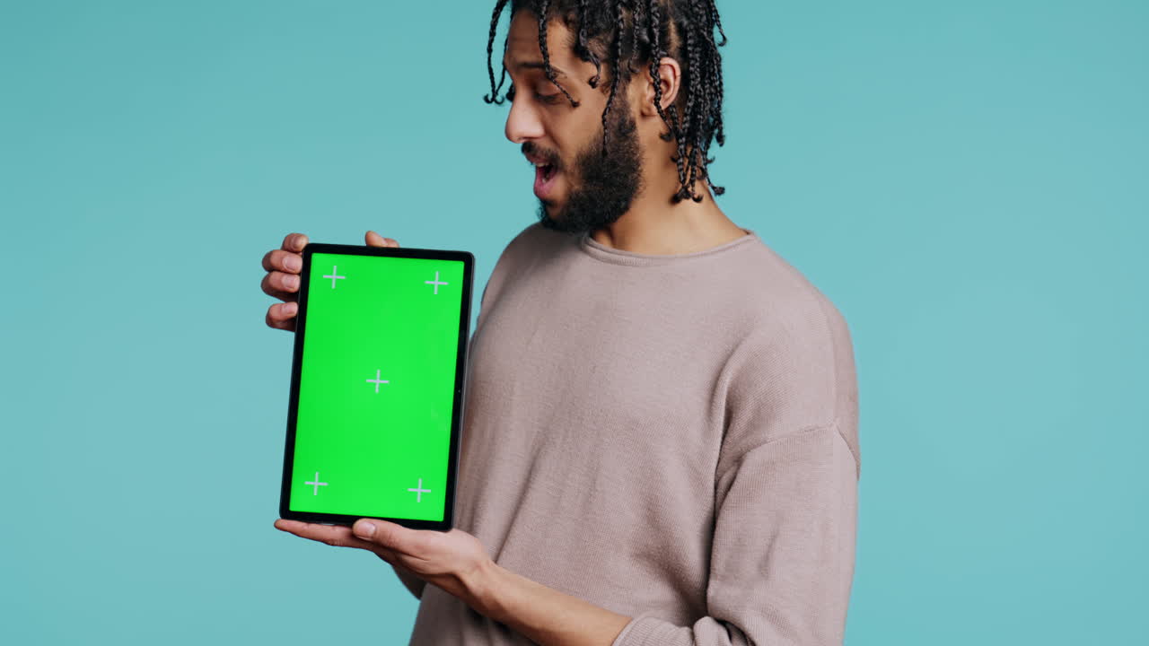 Man holds green screen tablet, showing positive emotion, studio background