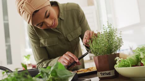 video of happy biracial woman in hijab taking care of plants