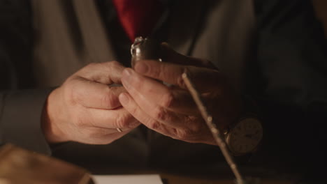 older passionate man evaluates an old silver skull watch in his office at night