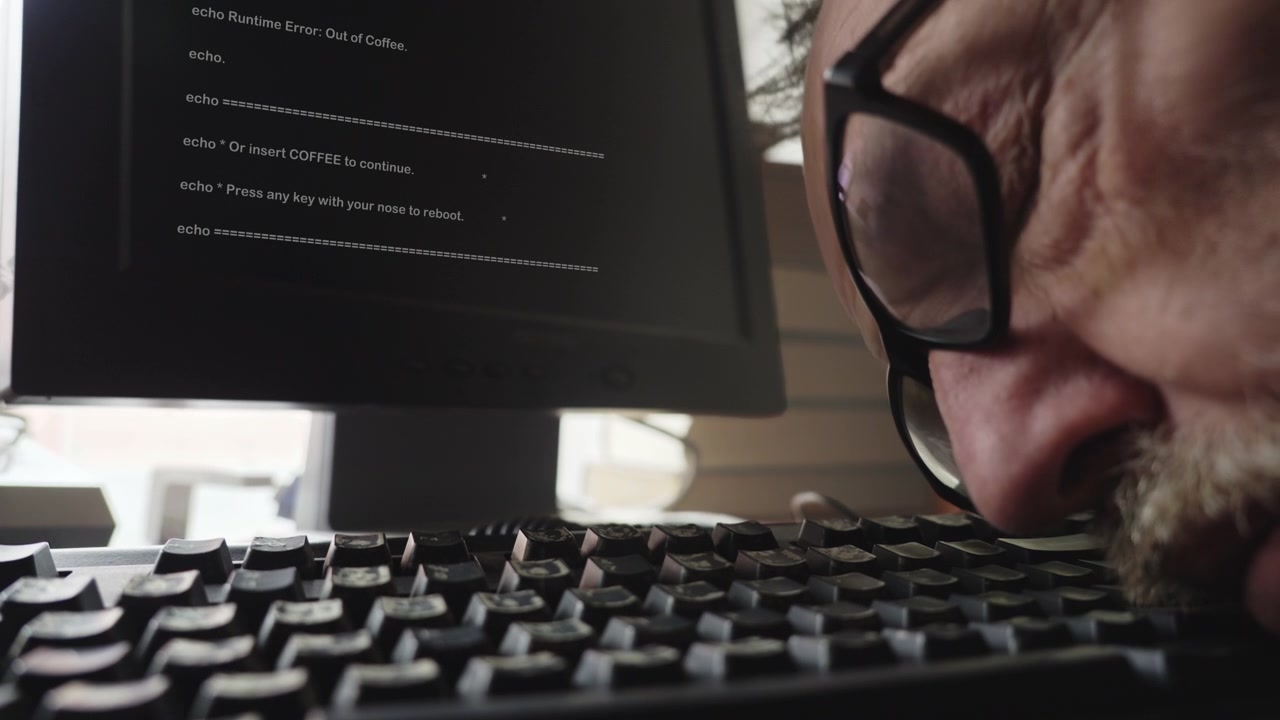 Close-up of a tired bearded man waking from sleep on a computer keyboard while work continues on-screen, symbolizing burnout, deadlines, stress, and workplace exhaustion.