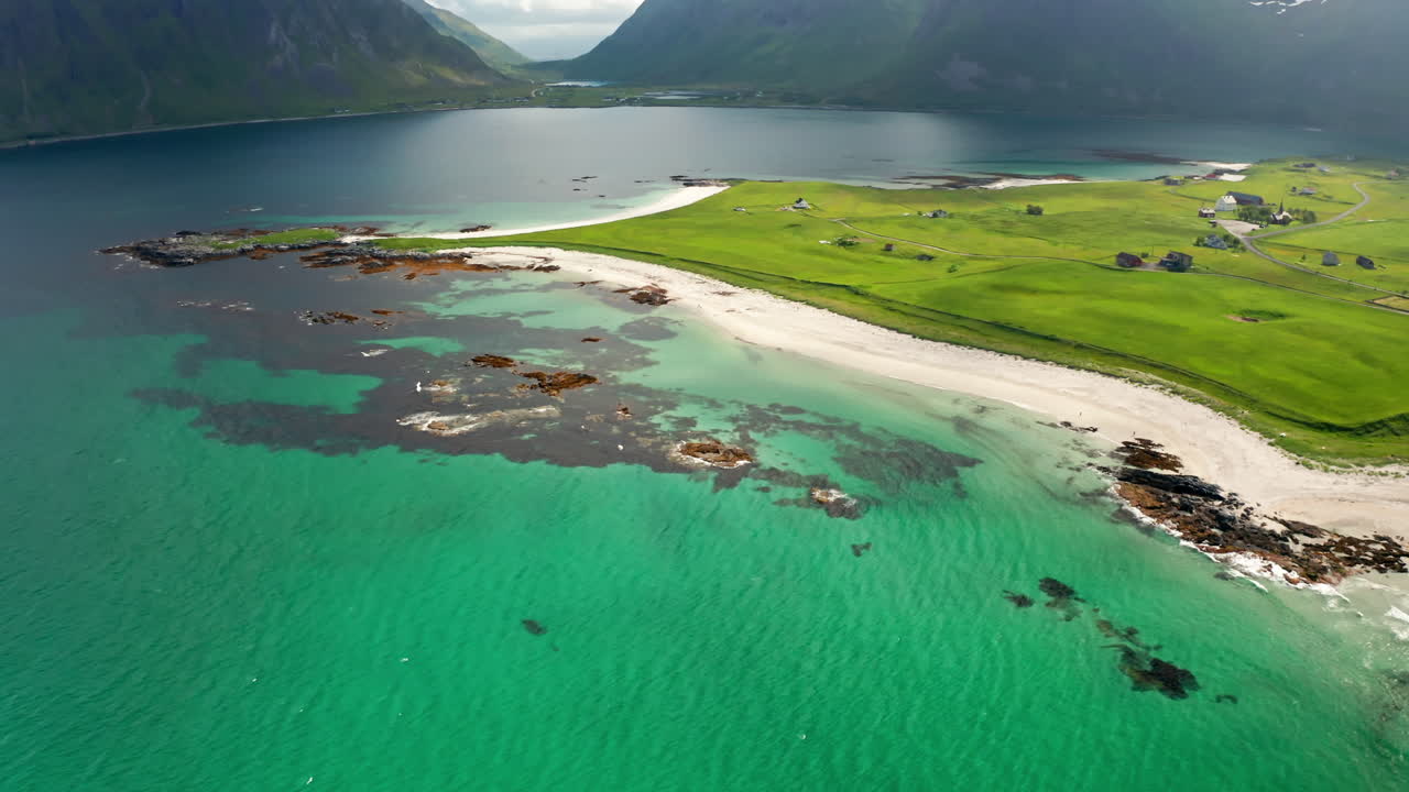 Aerial drone shot over the scenic Nordic Landscape of the Lofoten Islands in Norway. High view of green fields and the long stretching white sanded beach and the turquoise sea.