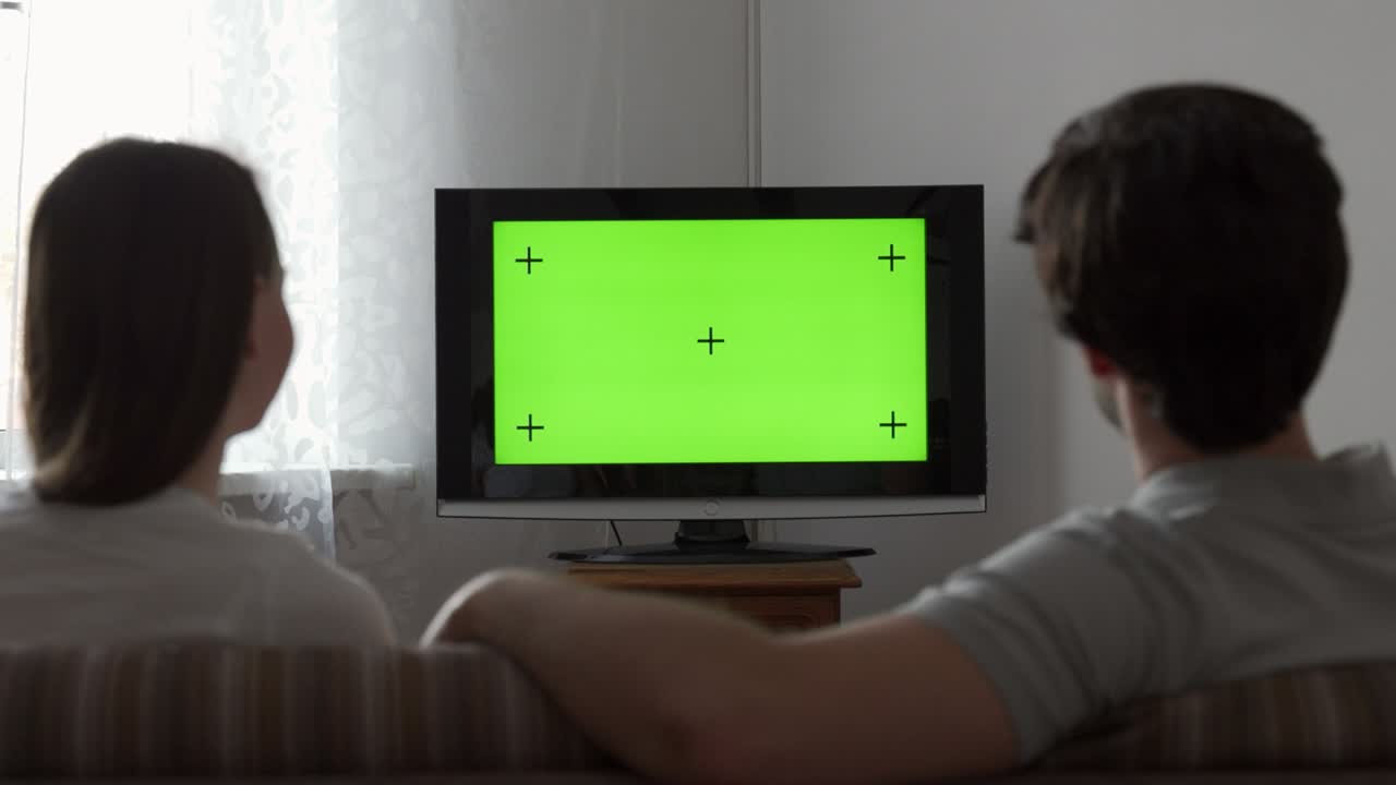 Couple watches green mock-up screen tv while sitting on a couch in the living room