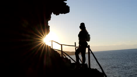 mujer joven con sombrero admira durante la puesta de sol, el paisaje que se encuentra en la costa del municipio de galdar en la isla de gran canaria y durante la puesta de sol