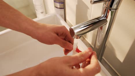 Man-washing-his-toothbrush-under-sink-in-bathroom