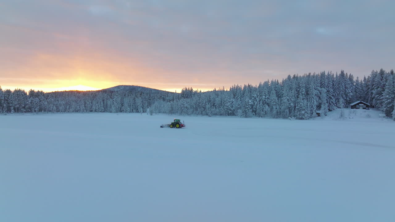 Luftfoto som sporer en Norbotten snøfreser som rydder en skogkledd vei med is og snøfokk under en gyllen soloppgang.