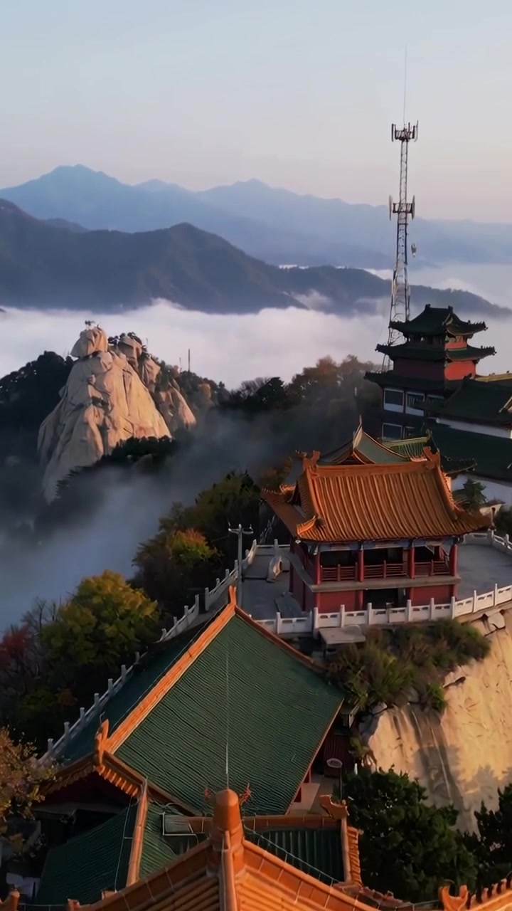 Video verticale: La telecamera si allontana, rivelando un tempio in cima alla montagna con tetti arancione-oro e nebbia