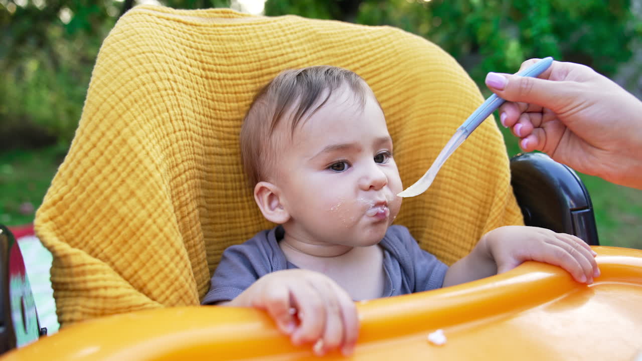 Adorable one-year old toddler eating porridge from spoon well. Nice kid eating food and smiling sweetly. Blurred backdrop.