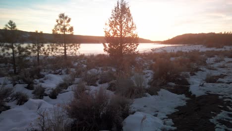 Wide-tilting-up-shot-of-a-frozen-lake-along-the-beach-at-sunset