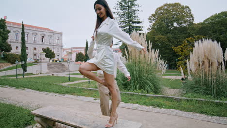 Energetic-pair-romantic-date-at-public-park.-Latina-happy-woman-dancing-on-bench