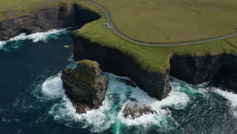 Aerial-view-of-boiling-water-at-coastal-rocks.-Amazing-shot-of-high-cliffs-and-green-grass-with-road-on-top.-Kilkee-Cliff-Walk,-Ireland