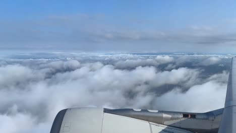 aerial view from airplane window over clouds with visible jet engine, daylight