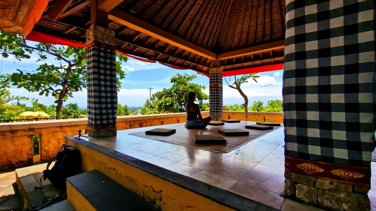 Person meditating in a traditional gazebo with scenic Bali views in the background