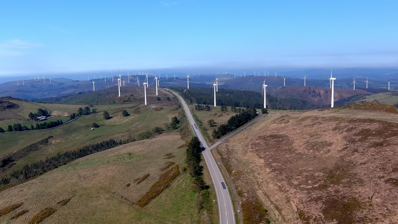 gran parque de turbinas eólicas en funcionamiento y una carretera de dos vías que cruza por el medio de los molinos de viento en una tarde soleada de cielo azul