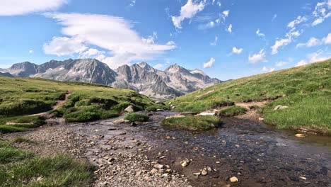 a pristine alpine stream flows across a grassy valley floor beneath the dramatic backdrop of pizzo rotondo in the lepontine alps, ticino, switzerland, on a bright summer afternoon