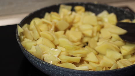 la mano del guante púrpura revuelve las papas en una sartén con una espátula de madera, cierra
