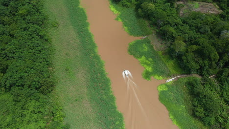 Filmado-Con-Un-Dron-Cinematográfico-Con-Un-Bote-Que-Baja-Por-El-Río-Amazonas-Y-La-Selva-Tropical-Que-Rodea-El-Río-En-Perú,-Inclinándose-Lentamente-Hacia-El-Bote