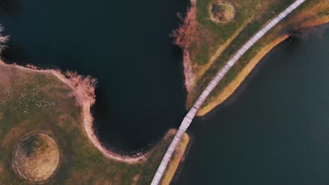 two persons walking over a wooden foothpath over a bridge between two blue lakes